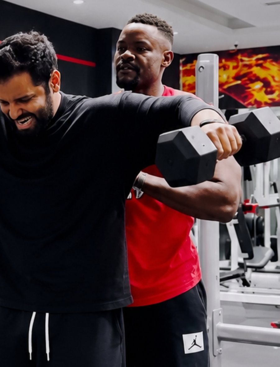 Coach Asim Mohammed coaching a client through a dumbbell press in a Dubai gym